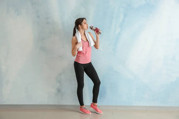 Sporty young woman with bottle of water near color wall — Stock Photo, Image