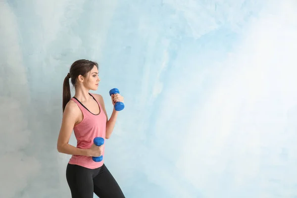 Sporty young woman with dumbbells on color background — Stock Photo, Image