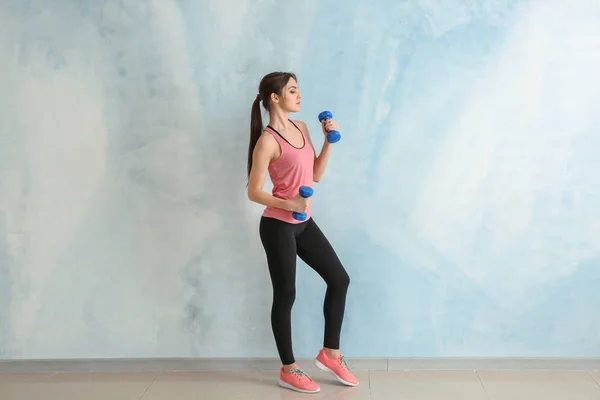 Sporty young woman with dumbbells near color wall — Stock Photo, Image