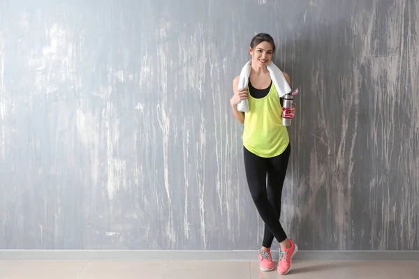 Sporty young woman with bottle of water near grunge wall — Stock Photo, Image