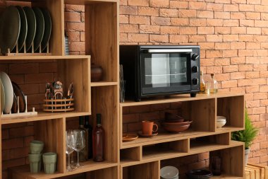 Set of clean dishes with utensils and microwave oven on wooden shelves near brick wall clipart