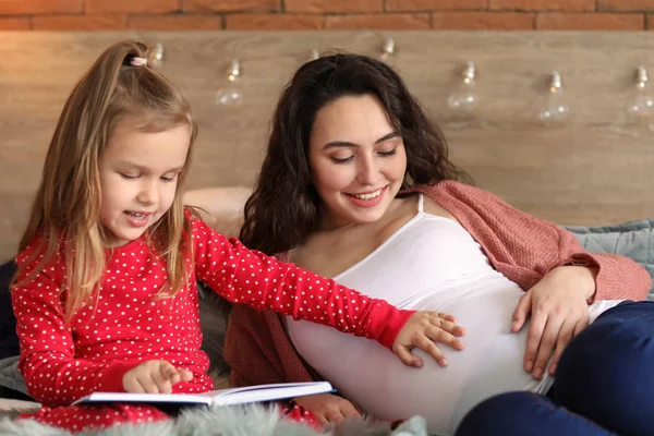 Madre embarazada con una hija pequeña leyendo un libro en casa — Foto de Stock