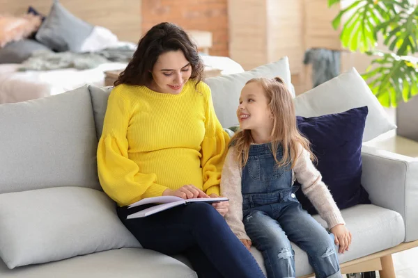 Pregnant mother with little daughter reading book at home — Stock Photo, Image