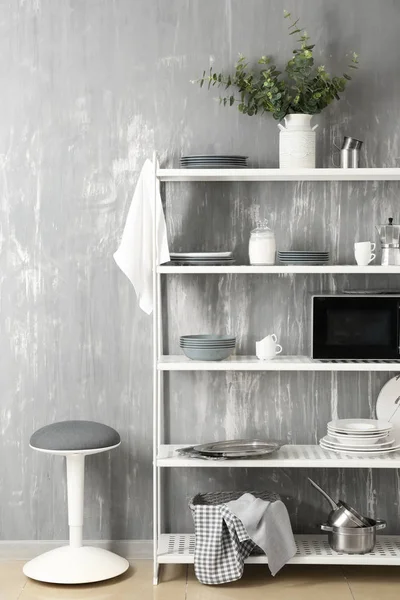 Set de platos limpios con utensilios y horno microondas en estantes cerca de la pared gris —  Fotos de Stock