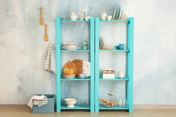 Set of clean dishes with utensils on shelves near light wall — Stock Photo, Image