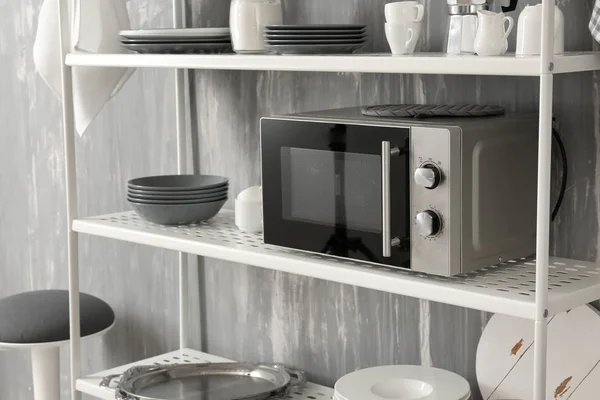 Microwave oven with clean dishes on shelves near grey wall