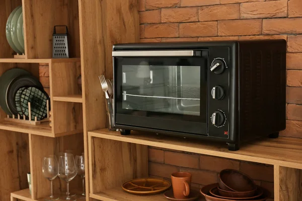 Microwave oven with clean dishes on wooden shelves near brick wall