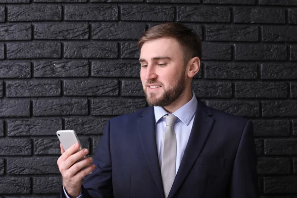 Retrato de hombre guapo con teléfono móvil sobre fondo de ladrillo oscuro — Foto de Stock