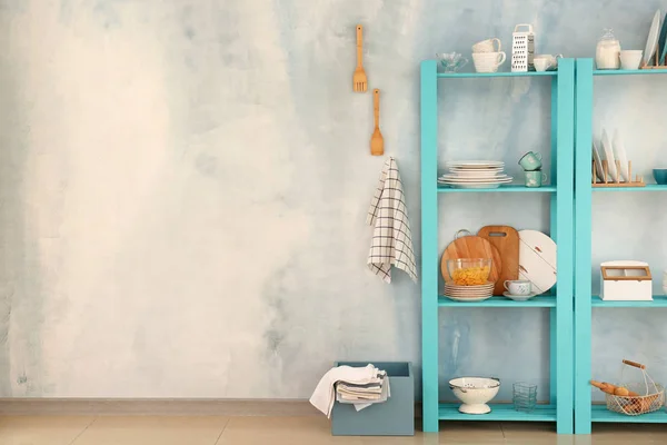 Set of clean dishes with utensils on shelves near light wall — Stock Photo, Image