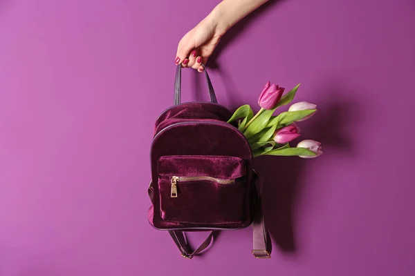 Vrouwelijke hand met rugzak en boeket tulpen op kleur achtergrond — Stockfoto