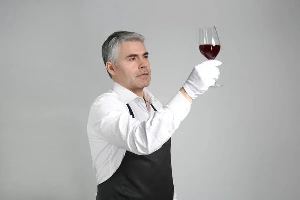 Sommelier maturo con bicchiere di vino su sfondo grigio — Foto Stock