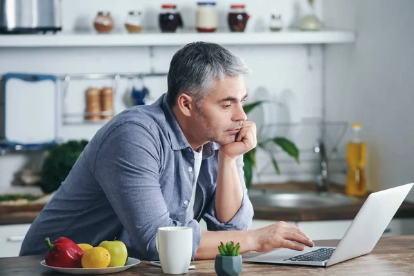 Volwassen man aan het werk op laptop in de keuken — Stockfoto