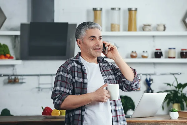 Volwassen man praten via de telefoon tijdens het drinken van koffie in de keuken — Stockfoto