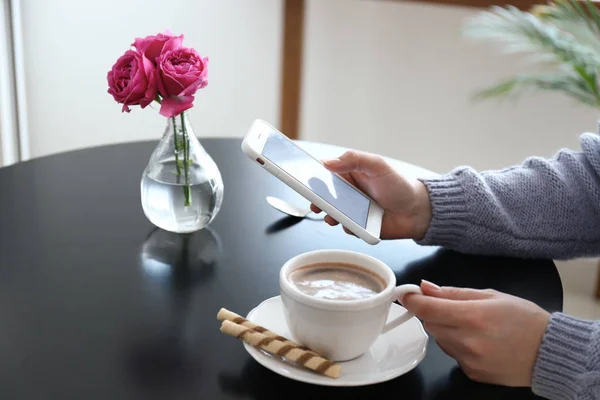 Młoda kobieta z telefonu komórkowego picia kawy w tabeli — Zdjęcie stockowe