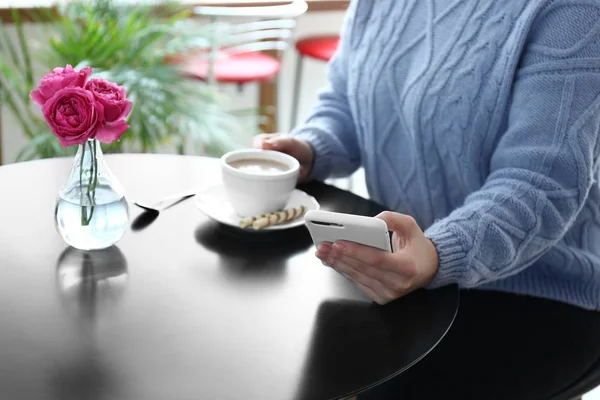 Jovem com telefone celular bebendo café à mesa — Fotografia de Stock