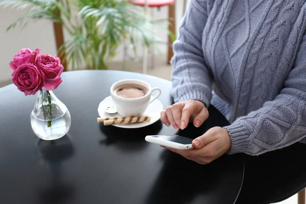 Young woman with mobile phone sitting at table — Stock Photo, Image