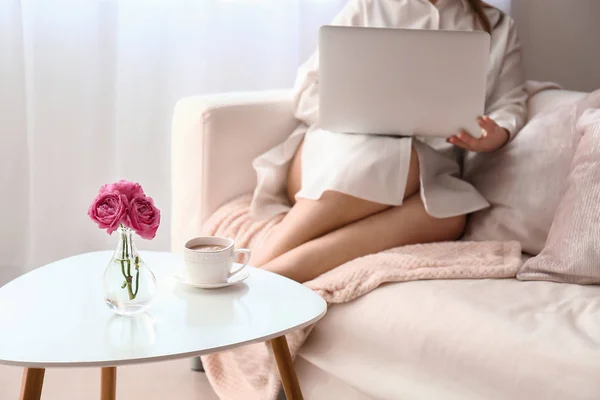 Jovem mulher usando laptop perto da mesa com xícara de café em casa — Fotografia de Stock