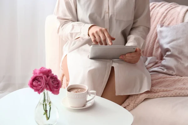 Jovem mulher usando tablet PC perto da mesa com xícara de café em casa — Fotografia de Stock