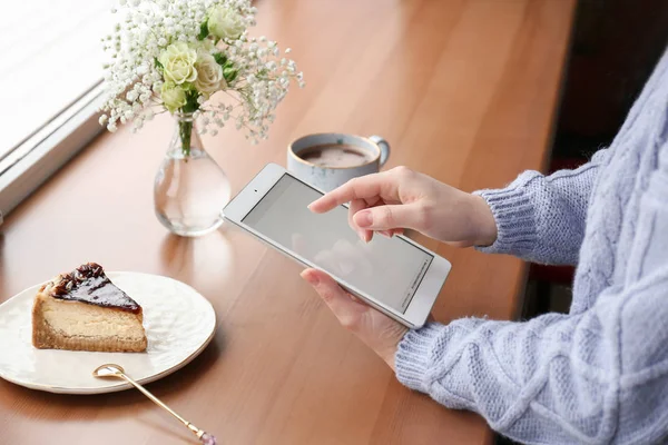 Νεαρή γυναίκα με το tablet Pc που κάθεται στο τραπέζι κοντά στο παράθυρο — Φωτογραφία Αρχείου