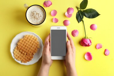 Cep telefonlu kadın eller ve arka planda bir fincan kahve.