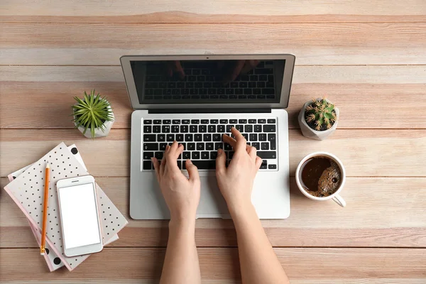 Женские руки с ноутбуком, мобильным телефоном и чашкой кофе на деревянном фоне — стоковое фото