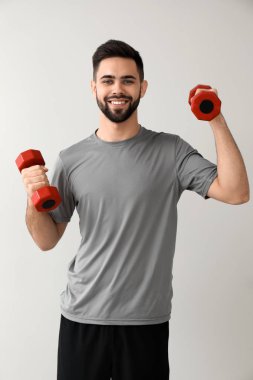 Işık arka plan üzerinde dumbbells ile sportif genç adam
