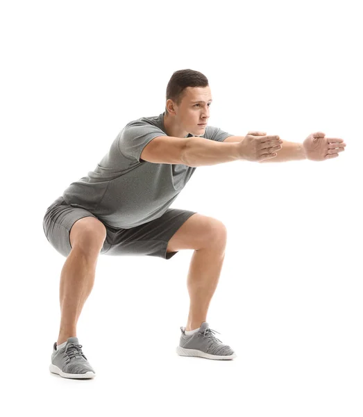 Sporty young man doing squats against white background — Stock Photo, Image