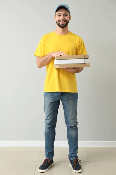 Jovem mensageiro com caixas de pizza perto da parede de luz — Fotografia de Stock