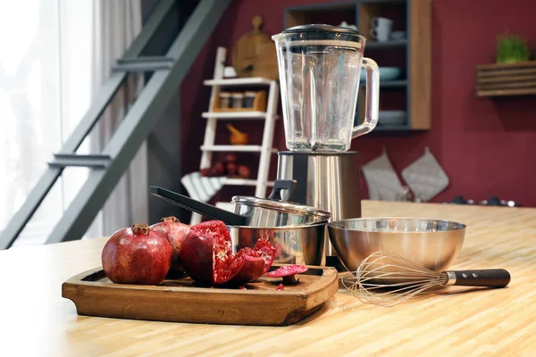 Blender, different utensils and pomegranates on table in kitchen — Stock Photo, Image