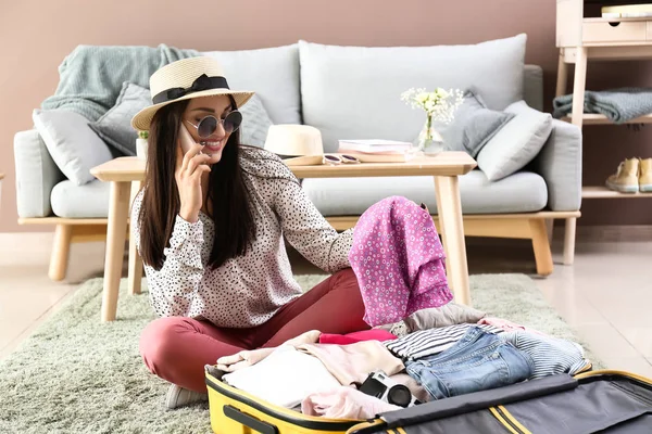 Mujer joven hablando por teléfono mientras empaca la maleta en casa. Concepto de viaje —  Fotos de Stock