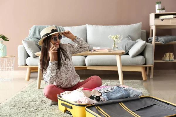 Młoda kobieta rozmawia przez telefon podczas pakowania walizki w domu. Koncepcja podróży — Zdjęcie stockowe