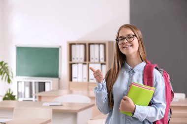 Şirin kız öğrenci gösteren başparmak-up sınıfta
