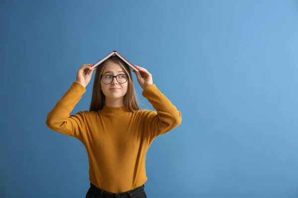 Schoolgirl with book on color background — Stock Photo, Image