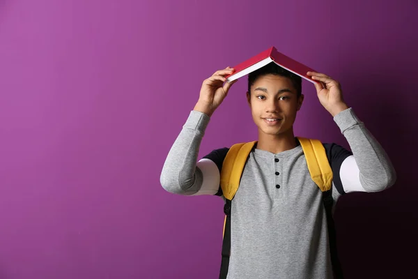 Colegial afroamericano con libro sobre fondo de color —  Fotos de Stock