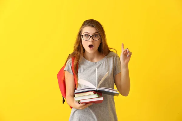 Emotioneel schoolmeisje met boeken en verhoogde wijsvinger op kleur achtergrond — Stockfoto