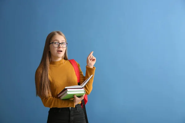 Schoolgirl with books and raised index finger on color background — Stock Photo, Image