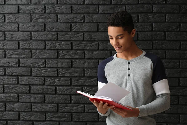 African-American schoolboy with book on dark background — Stock Photo, Image