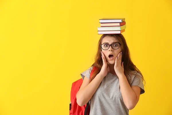 Colegiala conmocionada con libros sobre fondo de color — Foto de Stock