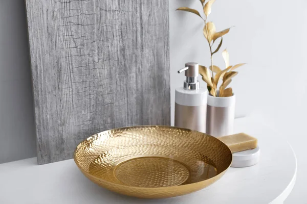 Golden bowl with water and cosmetics on table in bathroom — Stock Photo, Image