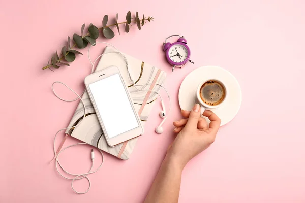 Female hand with cup of coffee, mobile phone, notebook and clock on color background — Stock Photo, Image