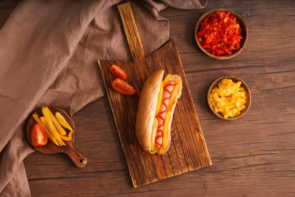 Board with tasty hot dog on wooden table — Stock Photo, Image