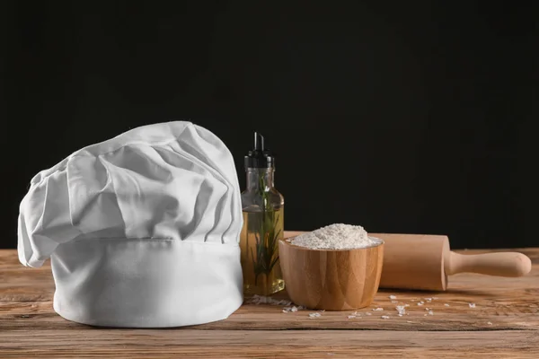 Composition with chef's hat on wooden table against dark background — Stock Photo, Image