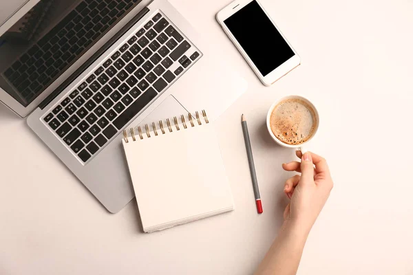 Női kéz, csésze kávéfőző, laptop, jegyzetfüzet és mozgatható telefon-ra könnyű háttér — Stock Fotó