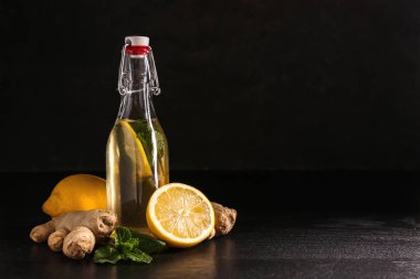 Koyu arka plana karşı masada limon ve zencefil ile lezzetli bir içecek şişe