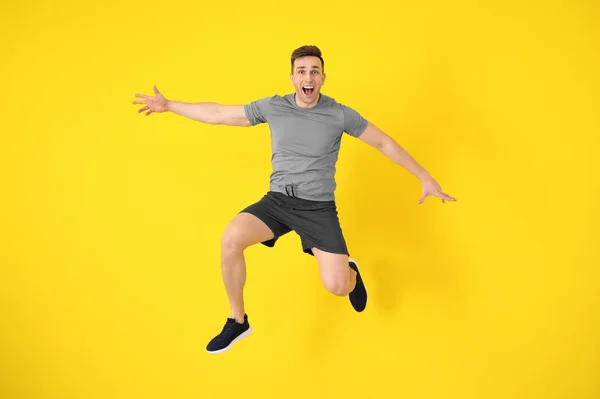 Young sporty man jumping against color background — Stock Photo, Image