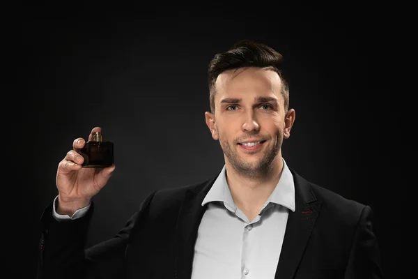 Handsome man with bottle of perfume on dark background — Stock Photo, Image