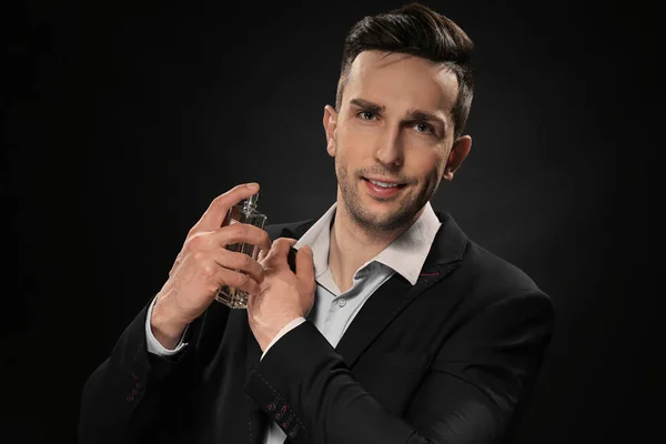 Handsome man with bottle of perfume on dark background — Stock Photo, Image