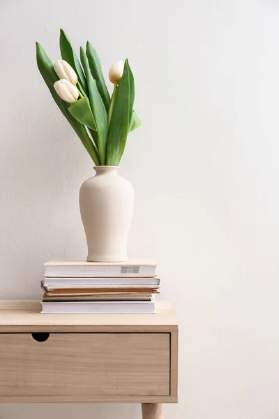 Vaas met boeket bloemen en boeken op tafel tegen lichte achtergrond — Stockfoto