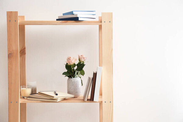 Vase with flowers and books on wooden shelf