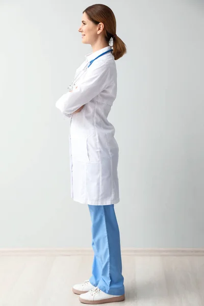 Beautiful female doctor near light wall — Stock Photo, Image